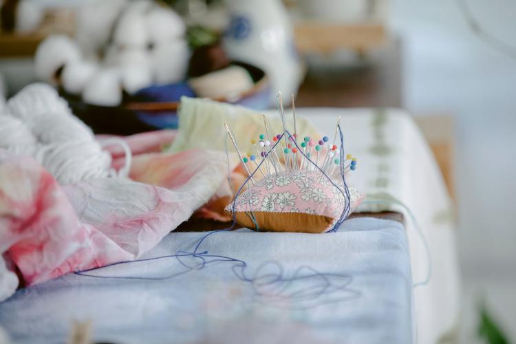 Photo d'une table sur laquelle repose des tissus, un coussin rempli d'aiguille